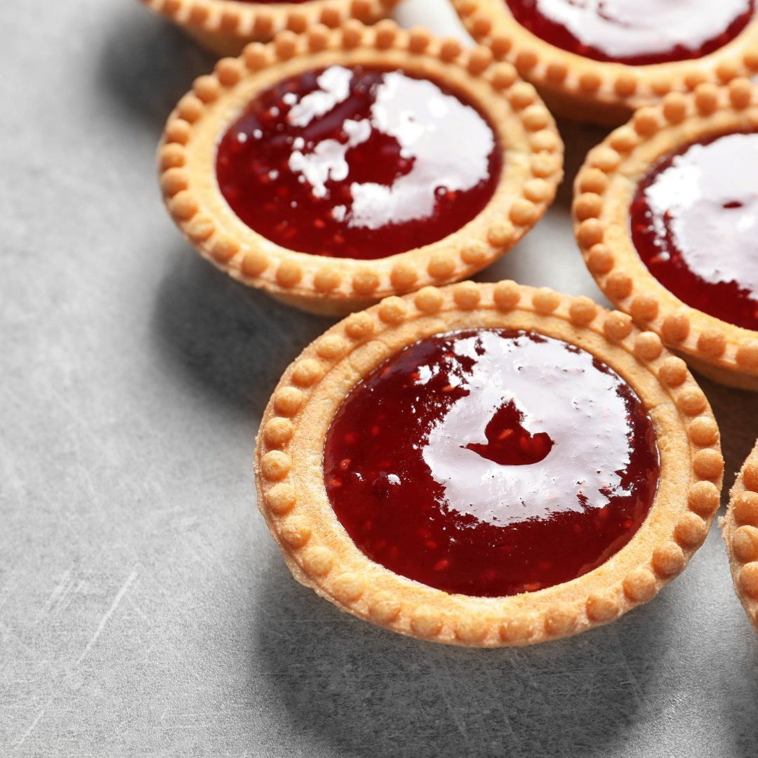 Tartelettes dorées garnies de confiture rouge, disposées sur une surface grise